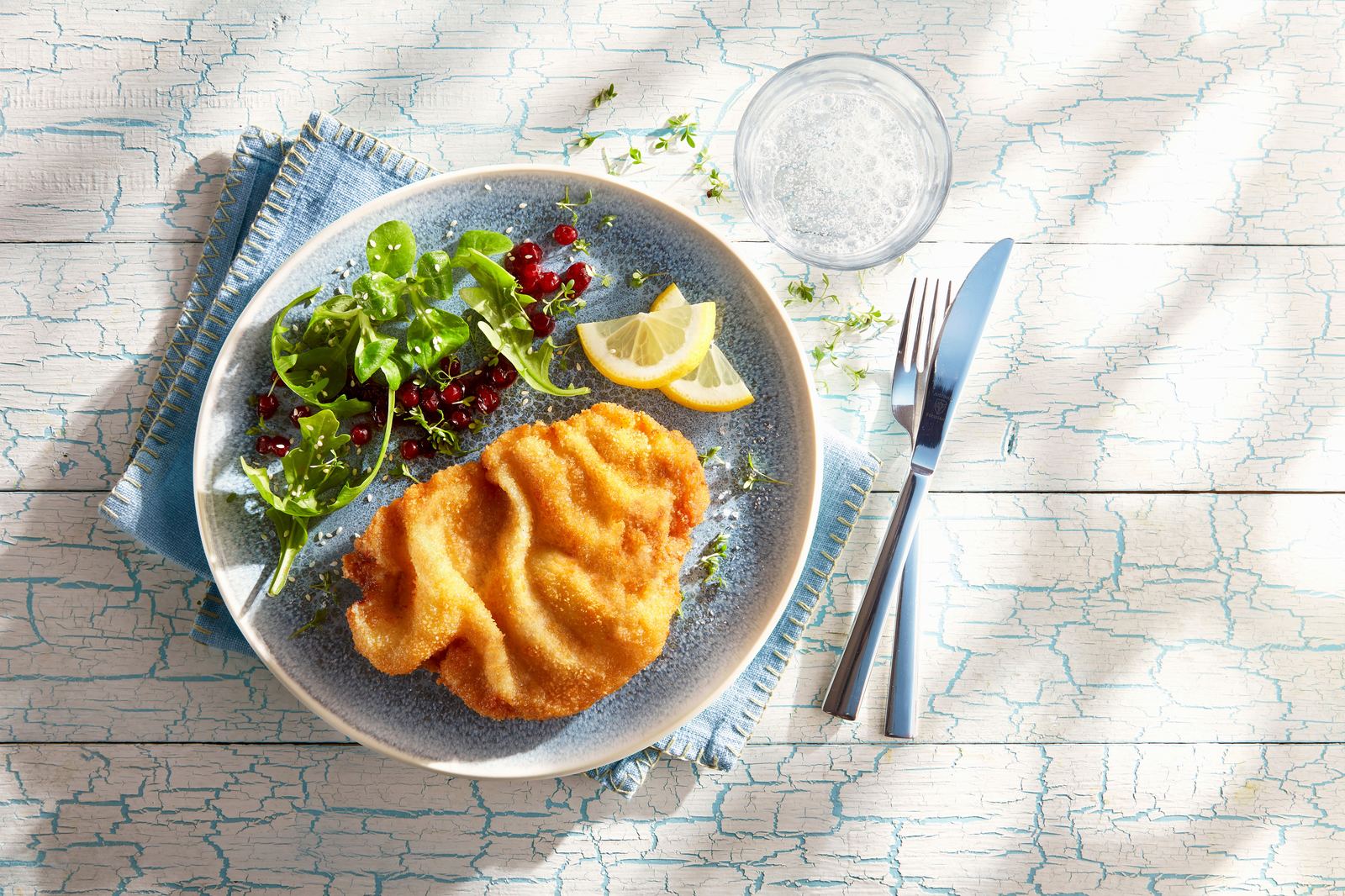 Goldbraun paniertes Schnitzel mit Salat und Zitrone auf einem blauen Teller